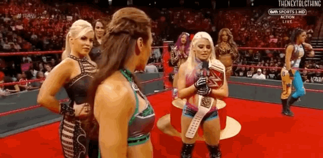 a group of women are standing in a wrestling ring and one of them is holding a championship belt .