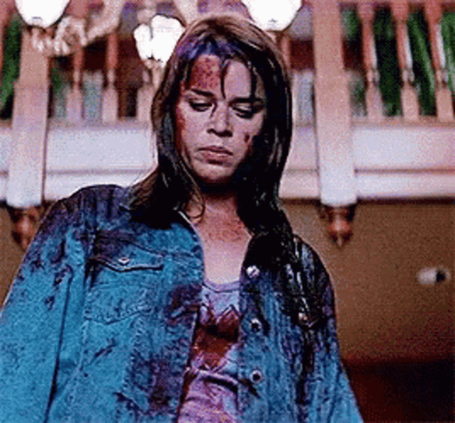 a woman in a blue denim jacket with blood on her face is standing in a room .