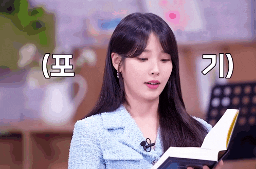 a woman in a blue jacket is reading a book with korean writing on the bottom