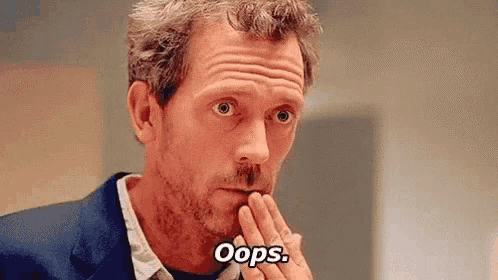 a man in a suit and tie is covering his mouth with his hand and saying `` oops '' .