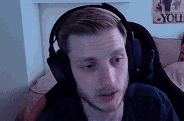 a man wearing headphones looks at the camera with a poster on the wall that says ' one piece ' on it