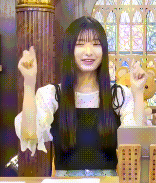 a young woman with long hair is sitting at a table with her arms in the air .
