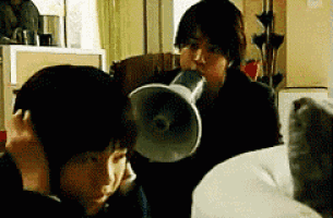a person is holding a megaphone in front of their ear while another person looks on .