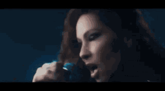 a woman is singing into a microphone in a dark room with a blue light behind her .