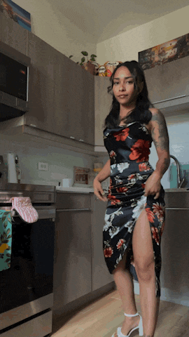 a woman in a floral dress is standing in a kitchen with a sign that says open