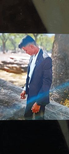 a young man in a suit leans against a tree