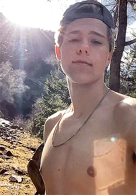 a shirtless young man wearing a baseball cap and a necklace