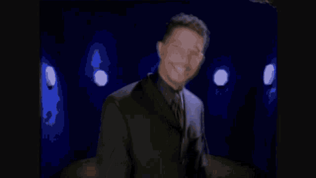 a man in a suit is laughing with his arms outstretched in front of a blue wall .