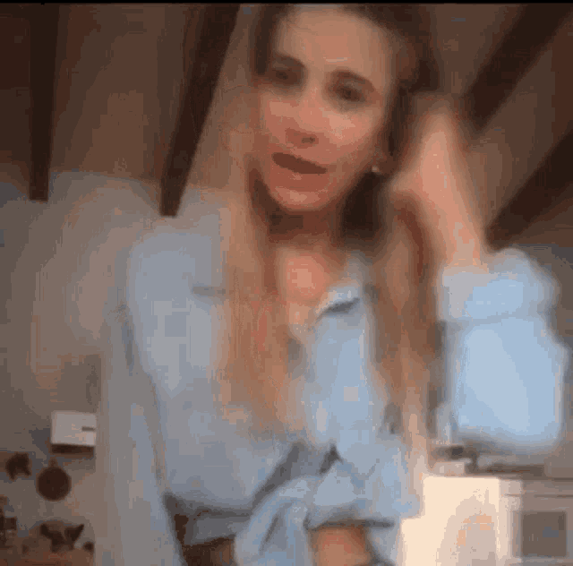 a woman in a blue shirt is standing in a kitchen with her hands on her head .