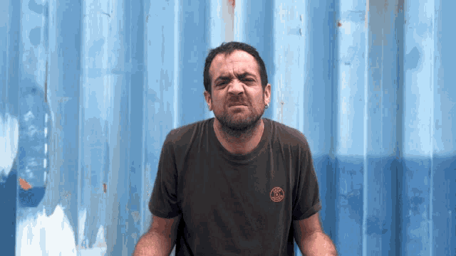 a man wearing a black t-shirt with a circle logo on the front making a funny face