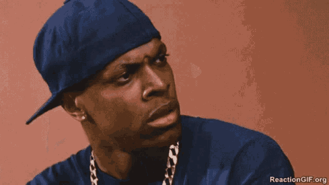 a man wearing a blue hat and a gold chain is smoking a cigarette .