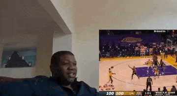a man is sitting in front of a large screen watching a basketball game .