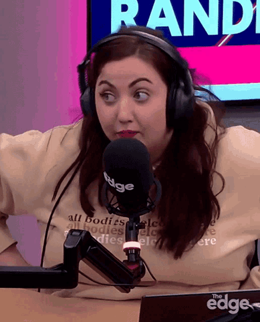 a woman wearing headphones stands in front of a microphone with the word randy on the screen behind her