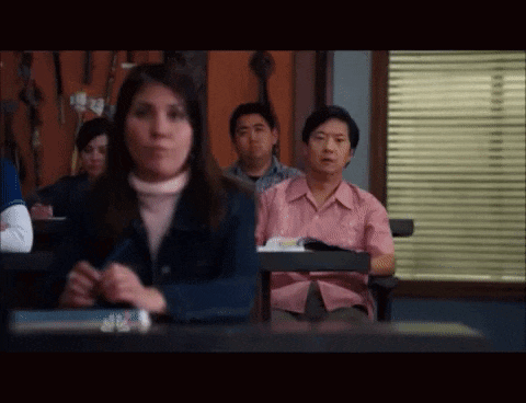 a group of people are sitting in a classroom with a man in a pink shirt