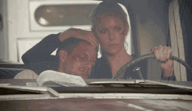a woman is holding a man 's head while driving a vehicle