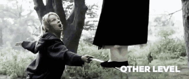 a woman is holding a knife while standing next to a tree in a forest .