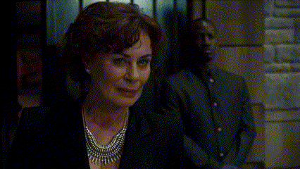 a woman wearing a silver necklace is smiling in front of a man in a suit .