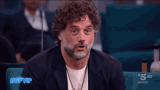 a man with curly hair and a beard is sitting in front of a screen that says 5 hd