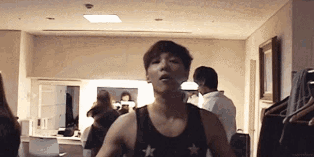 a man in a tank top is standing in a room with a woman standing behind him .