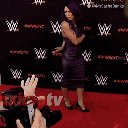 a woman in a purple dress is standing on a red carpet in front of a wall with wrestlers on it .