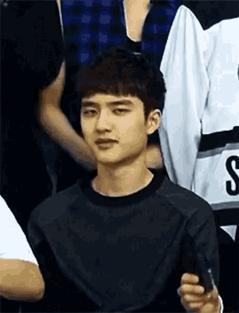 a young man is holding a cell phone in his hand while sitting in a crowd .