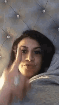 a woman is laying on a bed making a funny face and giving the middle finger .