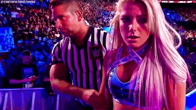a woman in a striped shirt is standing next to a referee in a wrestling ring .