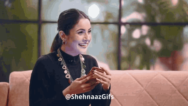 a woman sitting on a couch holding a cell phone with the hashtag @sehnaazgifs
