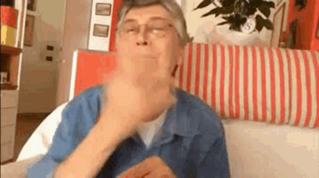an elderly woman wearing glasses is sitting on a couch with a striped pillow .