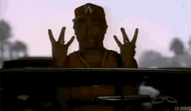 a man wearing a la hat is sitting in the driver 's seat of a car .