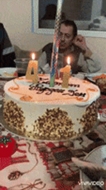 a man sitting at a table with a birthday cake with candles on it