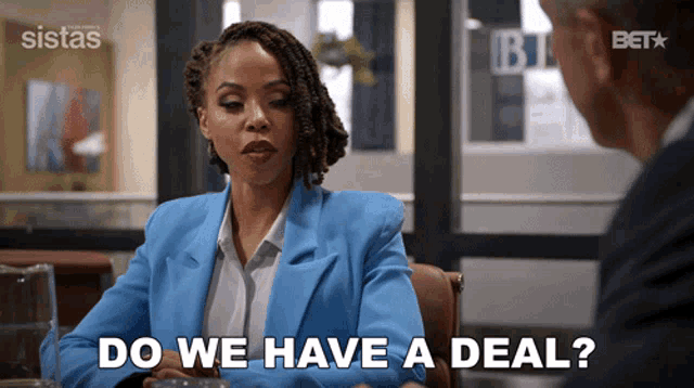 a woman in a blue jacket is sitting at a table with a man and says do we have a deal