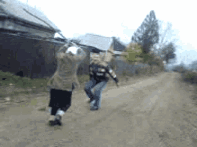 two people are walking down a dirt road and one is holding a stick