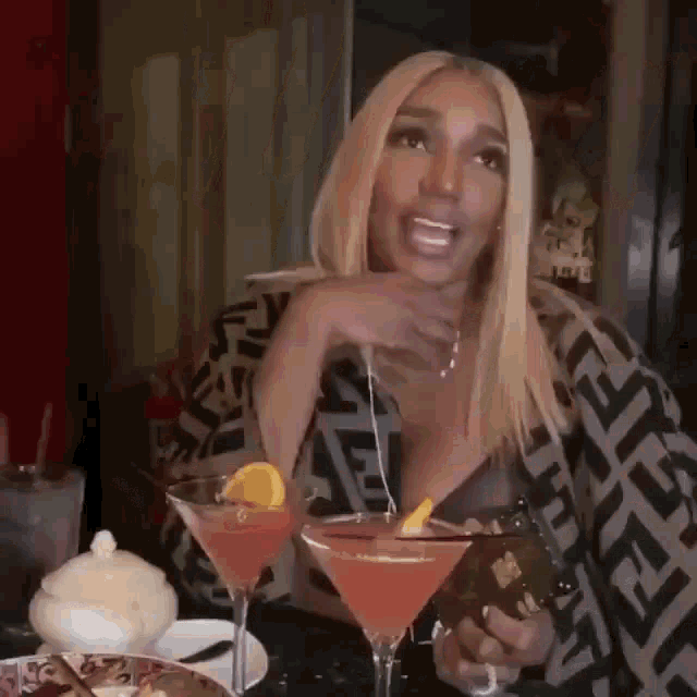 a woman is sitting at a table with two martini glasses and a bottle of wine .