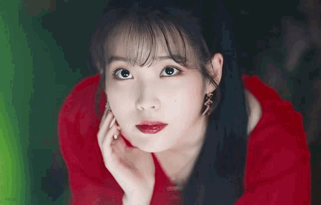 a woman in a red dress is looking at the camera with her hand on her face