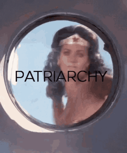 a woman in a wonder woman costume is looking out of a window with the word patriarchy written on it .