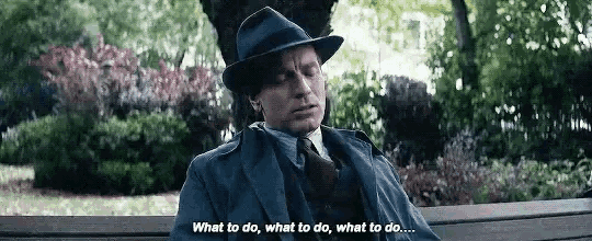 a man in a suit and hat is sitting on a bench in a park and talking to himself .