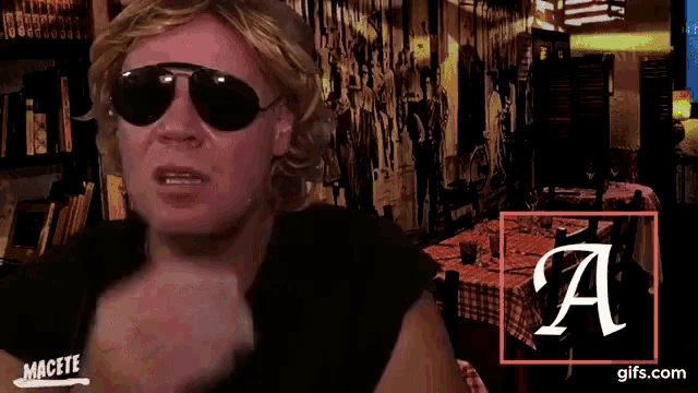 a man wearing sunglasses and a black shirt with the letter a on the bottom right