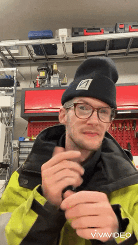 a man wearing glasses and a beanie with the letter a on it is in a garage