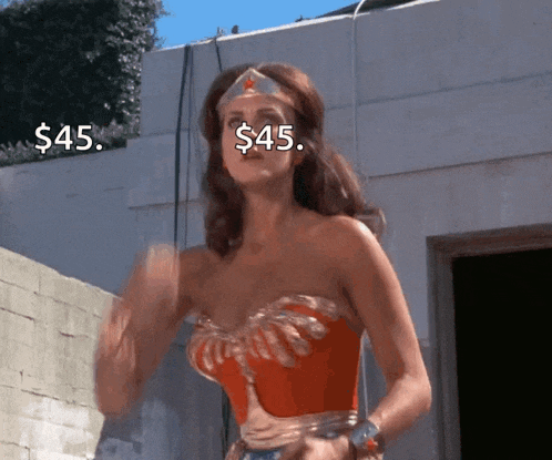 a woman in a wonder woman costume is standing in front of a building with $ 45 written on her face