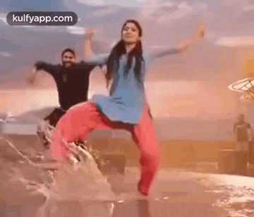 a man and a woman are dancing in the water on the beach .