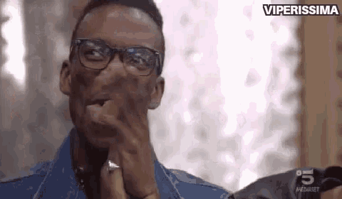 a man wearing glasses and a ring on his finger is covering his mouth with his hand .