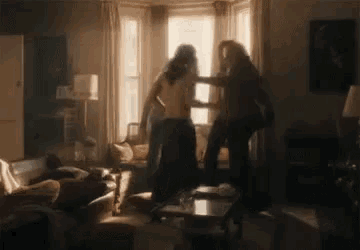 two people are fighting in a living room with a couch and a table .