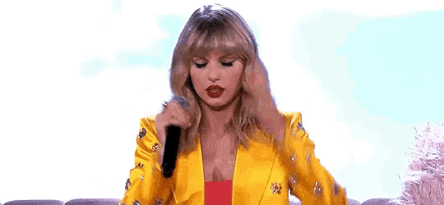 taylor swift is wearing a yellow jacket and red top and holding her head .