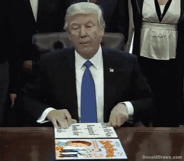 donald trump is sitting at a table holding a magazine that says donald draws.com