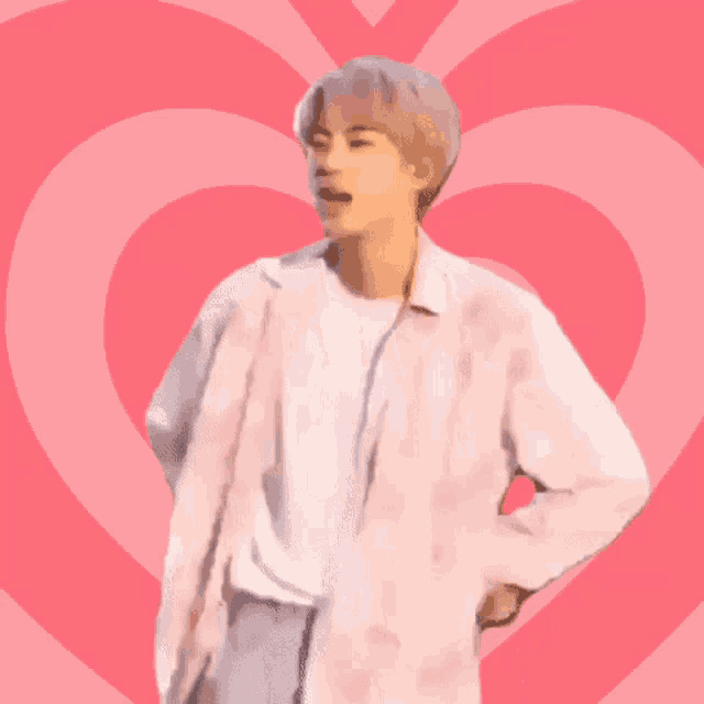 a man in a white shirt stands in front of a pink heart .