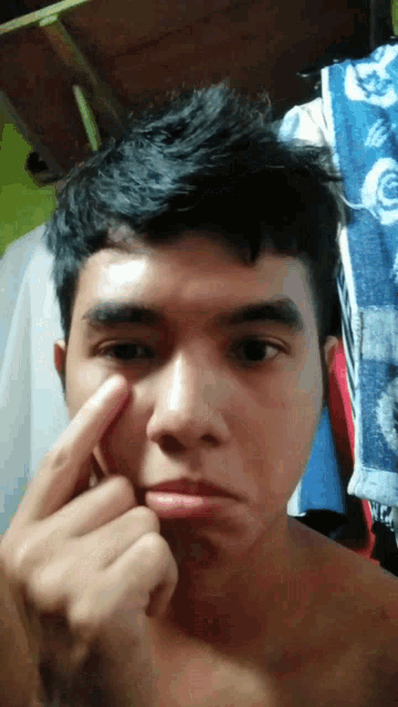 a man without a shirt is touching his face with his finger .