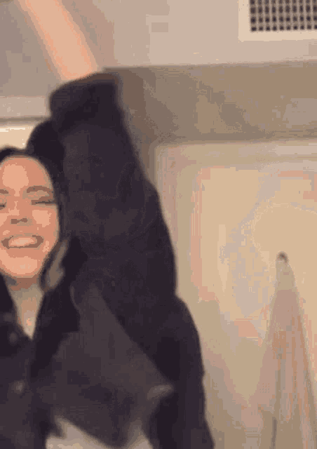 a woman in a black jacket is standing in a room with her arms in the air .