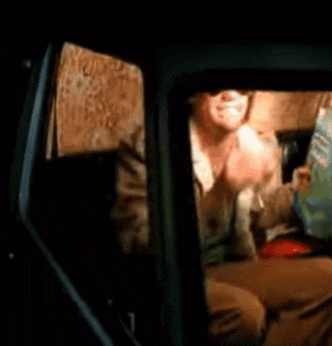 a man is sitting in a car eating a sandwich and drinking a beer .
