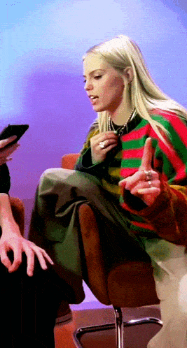 a woman in a striped sweater is sitting in a chair and pointing